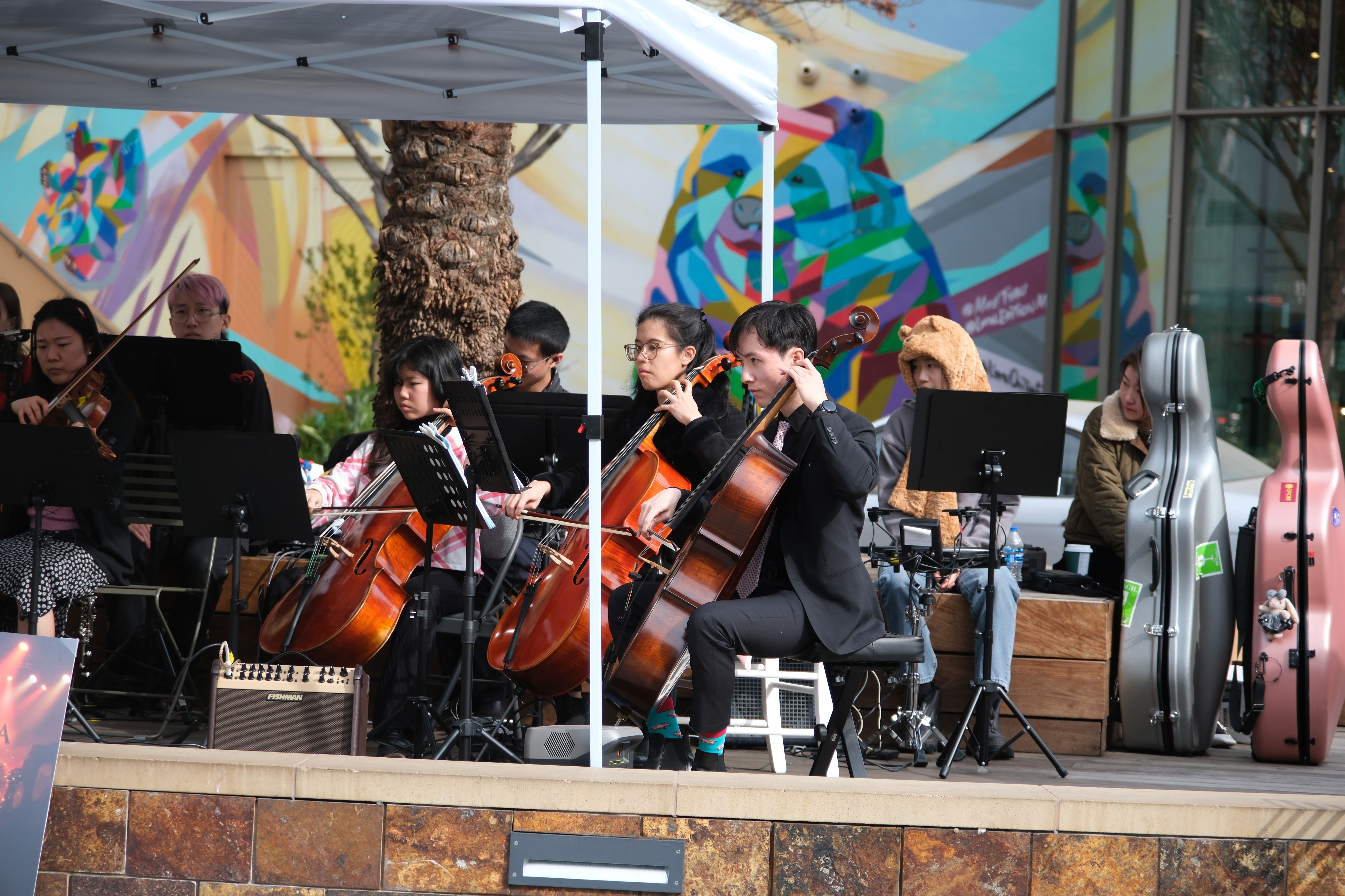 Cello section performing on stage with colorful mural backdrop at Santana Row